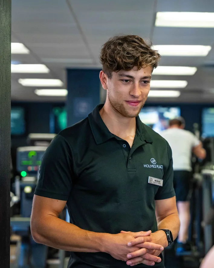 Marius Grek, coach sportif en polo Holmes Place, échange avec une cliente dans une salle de fitness